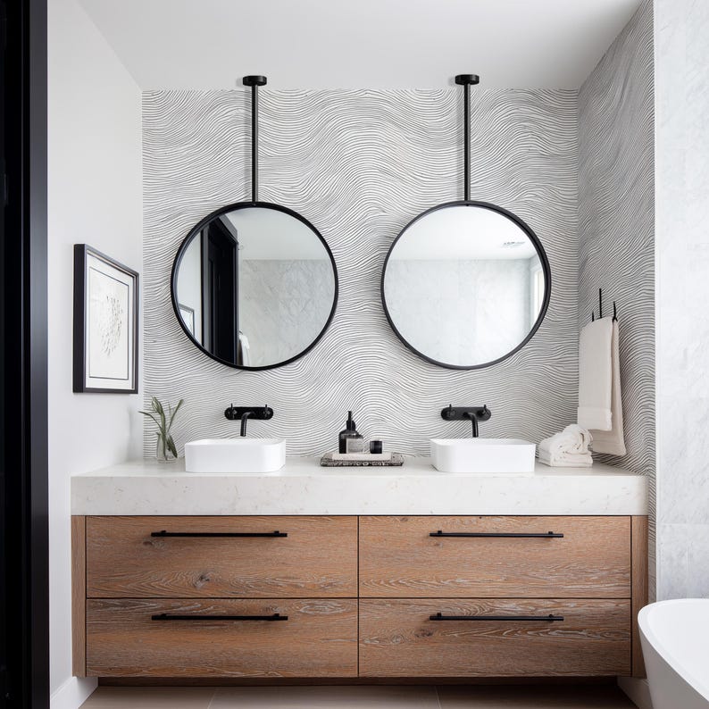 May include: A modern bathroom vanity with two round, black-framed mirrors suspended from the ceiling. The vanity features a light wood cabinet with four drawers, white countertops, and two white rectangular sinks. The background has a wavy, black and white patterned wallpaper.