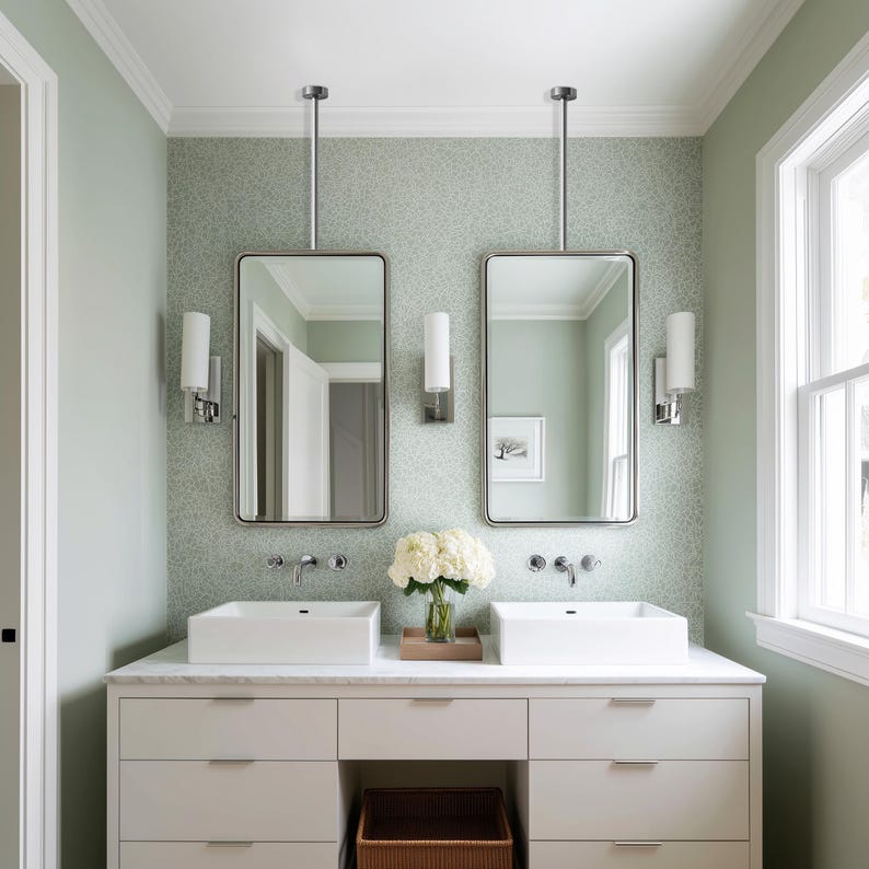 Op de afbeelding: Een moderne badkamer met twee rechthoekige spiegels die aan het plafond hangen. Elke spiegel wordt gecombineerd met een cilindrische wandlamp. De kamer heeft een dubbele wastafel met twee witte wastafels, een wit aanrechtblad en een lichtgroene muur.