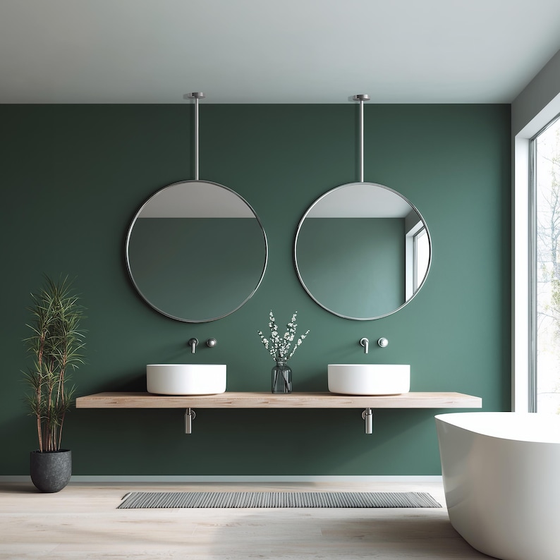 May include: A modern bathroom with a deep green wall, featuring two round mirrors suspended from the ceiling. White sinks sit on a wooden shelf, with a bathtub and a tall plant in the corner. The room has a minimalist design.