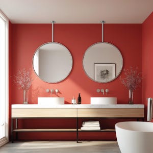 May include: A modern bathroom with a red wall, featuring two round mirrors suspended from the ceiling. The vanity has a light wood finish with a marble countertop and two white sinks. Decorative vases with floral arrangements and a white bathtub complete the scene.