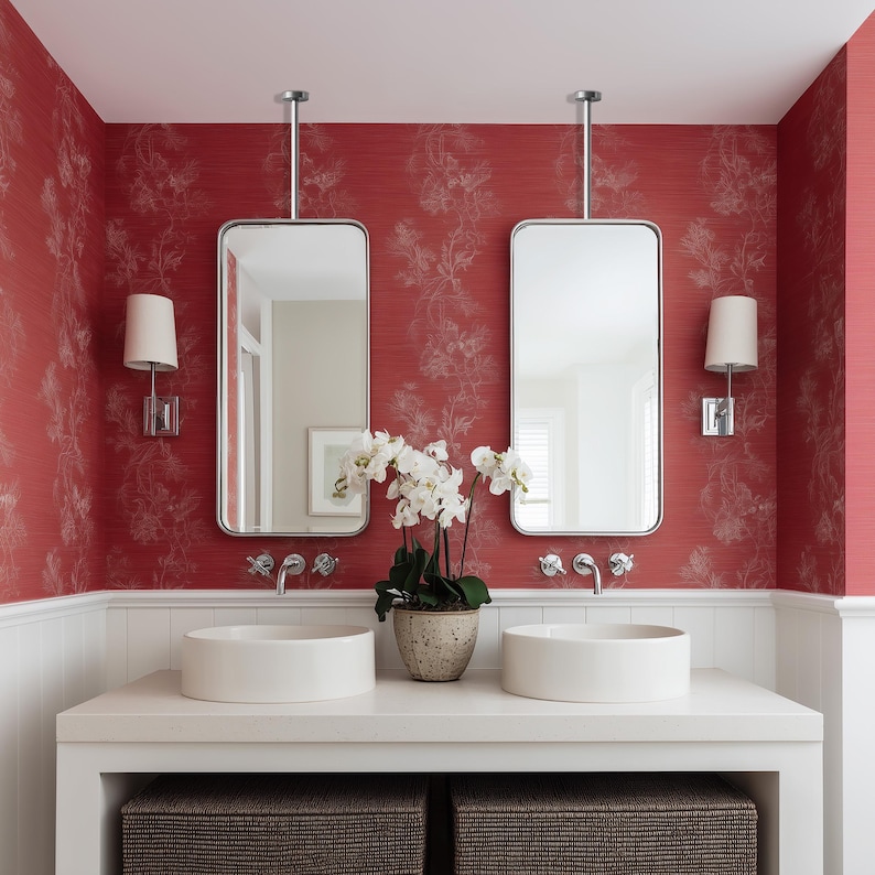 Op de afbeelding: Een moderne badkamer met rode bloemenbehang. Twee rechthoekige spiegels hangen boven een witte aanrecht met twee ronde wastafels. Een orchidee in een pot staat tussen de wastafels. Wandkandelaars en rieten manden maken het ontwerp compleet.