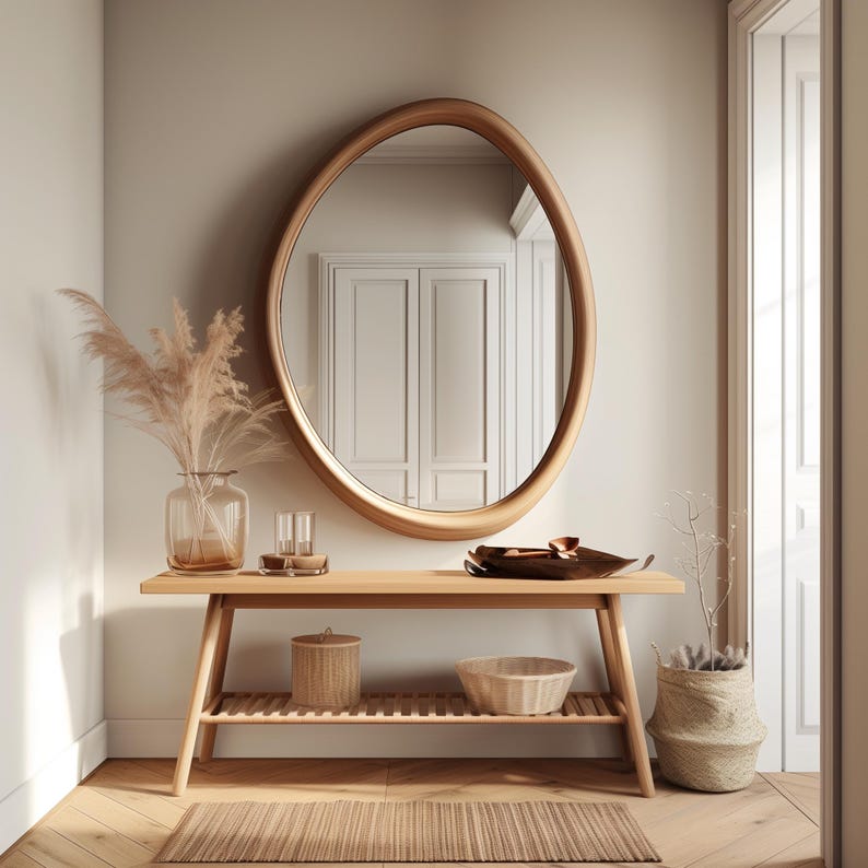May include: A wooden console table with a shelf, a round mirror, a vase with dried pampas grass, a bowl, and a woven basket. The table is in a hallway with light wood floors.