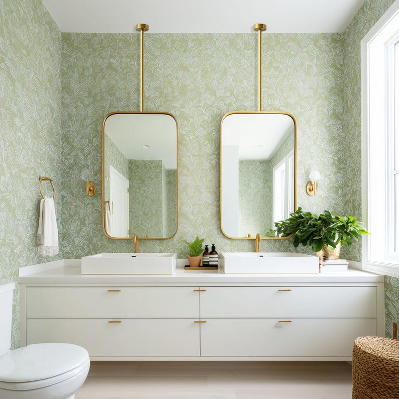 Op de afbeelding: Een moderne badkamer met een witte wastafel, twee rechthoekige spiegels met gouden frames en lichtgroen bloemenbehang. De spiegels hangen aan het plafond. De wastafel heeft twee witte wastafels en gouden kranen.
