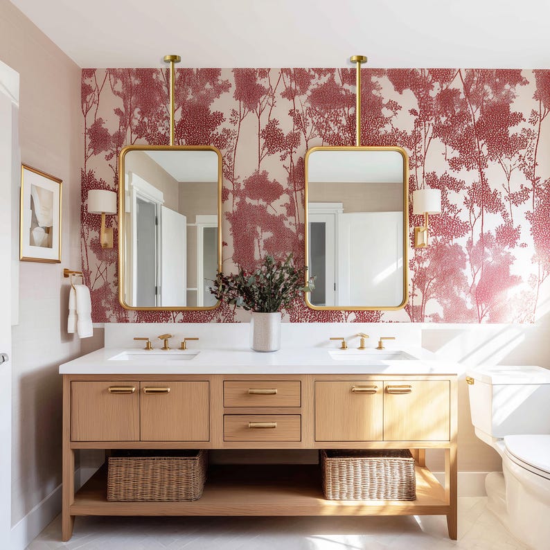 Op de afbeelding: Een moderne badkamer met een dubbele wastafel met een licht houten kast, een wit aanrechtblad en gouden armaturen. Twee rechthoekige spiegels hangen aan het plafond. Het behang heeft een rood boompatroon. Twee geweven manden staan onder de wastafel.