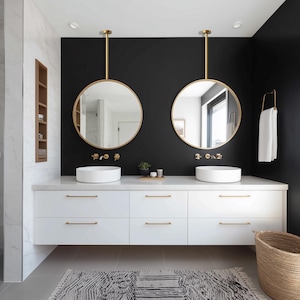 May include: A modern bathroom with a black accent wall, featuring two round gold-framed mirrors suspended above white vessel sinks. The white vanity has gold hardware, and a patterned rug sits on the floor. A woven basket and a towel rack complete the space.