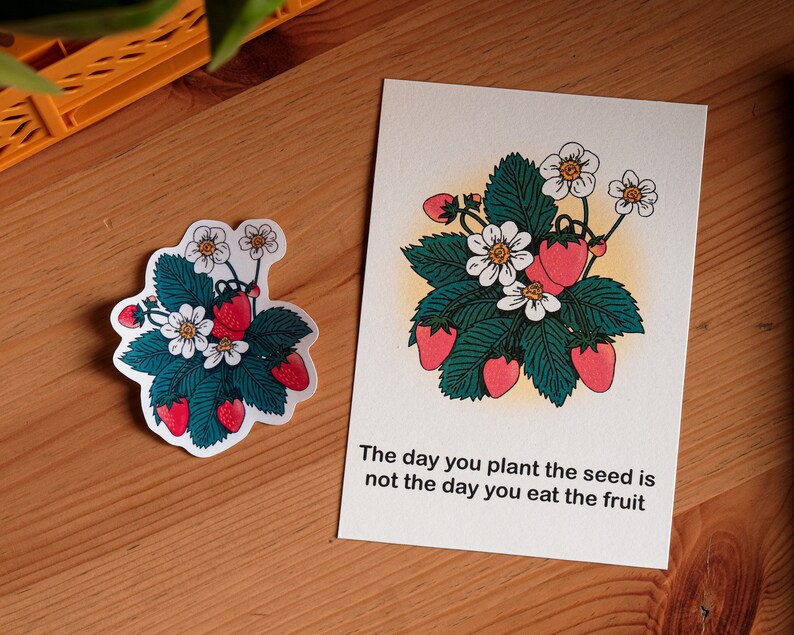 May include: A sticker and a card with a strawberry plant design. The illustration shows red strawberries, white flowers, and green leaves. The card reads: "The day you plant the seed is not the day you eat the fruit."