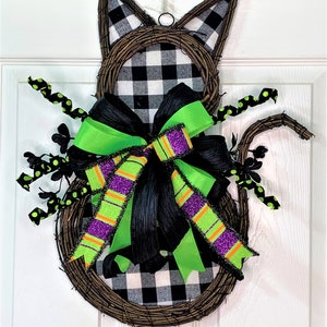 May include: A black and white checked cat-shaped wreath with a green and purple bow. The wreath is made of twigs and has black polka dot accents.