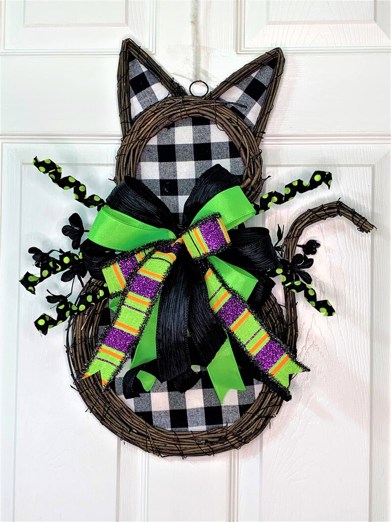 May include: A black and white checked cat-shaped wreath with a green and purple bow. The wreath is made of twigs and has black polka dot accents.