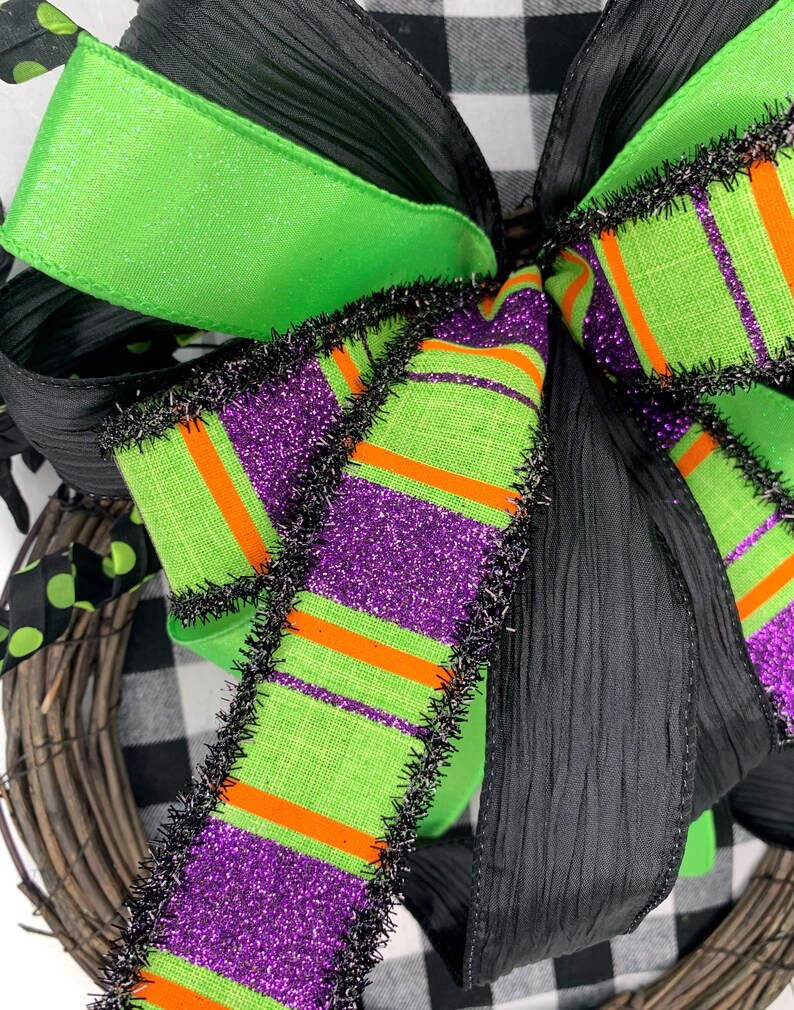 May include: A green, purple and orange striped ribbon with black fringe trim. The ribbon is tied into a bow with a black sheer ribbon.