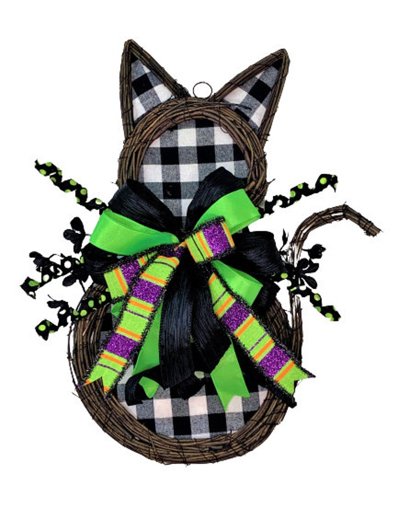 May include: A black and white checked cat-shaped wreath with a green and black bow. The wreath is made of twigs and has a black and white checked fabric covering the cat's body. The bow is made of green and black ribbon with purple and orange stripes.