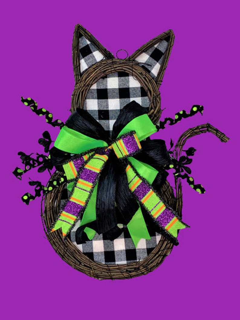 May include: A black and white checked cat-shaped wreath with a green and purple bow. The wreath is made of twigs and has black and white polka dot accents.