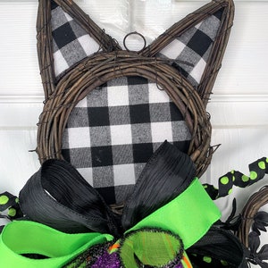 May include: Black and white buffalo check fabric wreath with black and green ribbon bow. The wreath is shaped like a cat's head with wire ears.