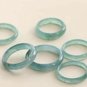 May include: Six jade rings in various sizes, all a pale green color. The rings are smooth and polished, with a subtle sheen.