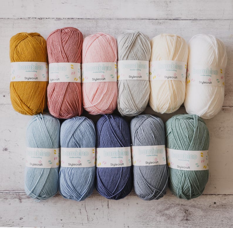 May include: Ten balls of yarn in various colors, including mustard yellow, dusty rose, pale pink, light gray, cream, white, light blue, denim blue, navy blue, and sage green. Each ball has a label that reads "bambino double knitting" and "Stylecraft".