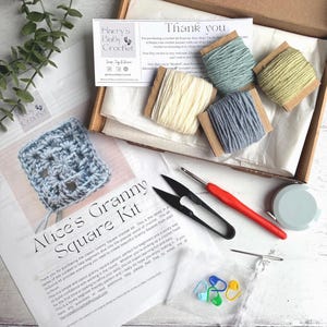 May include: A crochet kit in an open box, featuring various colored yarn spools, a crochet hook, scissors, stitch markers, and a measuring tape. The kit also includes a pattern for an Alice's Granny Square.
