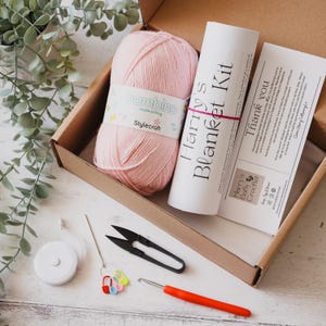 May include: A craft kit in a cardboard box, including pink yarn, a crochet hook, scissors, a measuring tape, stitch markers, and a tube labeled "Harry's Blanket Kit". The kit also contains a "Thank you" card.
