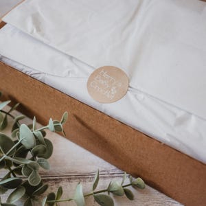 May include: A brown cardboard box with a white tissue paper lining. A brown circle sticker with the text "Harry's Baby Crochet" is on the tissue paper.