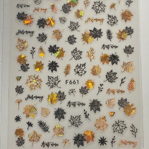May include: A sheet of gold and black nail decals with a fall theme. The decals feature leaves, branches, and the words "Autumn vibes" and "Harmony".