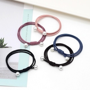 May include: Set of five hair ties with pearl accents. The hair ties are in black, brown, pink, and blue.