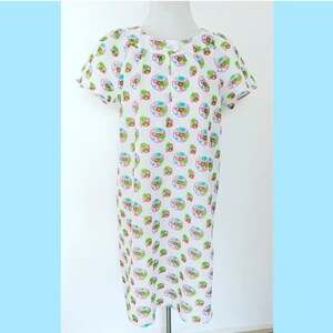 Puede incluir: Un vestido blanco con manga corta y cuello redondo. El vestido tiene un estampado colorido de círculos con detalles en verde, rosa y marrón.