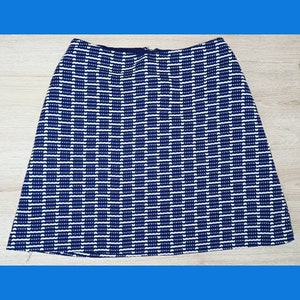 Puede incluir: Falda en forma de A con un patrón geométrico azul marino y blanco. La falda presenta un patrón repetitivo de rectángulos blancos sobre un fondo azul marino. La falda tiene cierre de cremallera y está hecha de tela tejida.