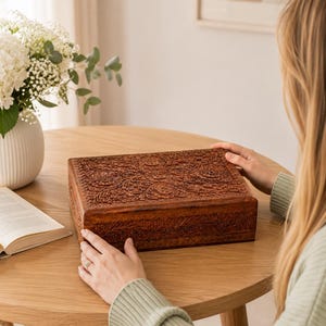 May include: A rectangular wooden box featuring intricate floral carvings on the lid and sides. The box is crafted from a medium-brown wood with a visible grain, showcasing detailed relief patterns of flowers and leaves across its entire surface.