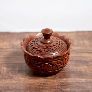 May include: A small, intricately carved wooden box with a lid. The box is brown and has a floral design. The lid has a knob on top.