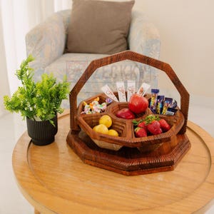 May include: A wooden serving tray with a handle, divided into six sections. The tray is filled with fruit, candy, and chocolate bars. The tray is on a wooden table.