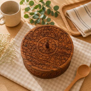 May include: A round wooden box with a lid featuring intricate floral carvings and a small central knob. The dark brown wood displays a natural grain pattern, and the detailed relief work covers both the top surface and the sides of the container.