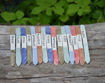 May include: A set of 15 ceramic plant markers with different herb names printed on them. The markers are decorated with a blue and green floral pattern and have a pointed end for easy insertion into the soil.