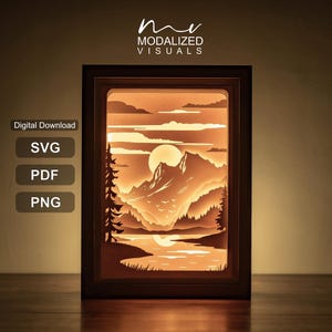 Peut inclure: Une boîte lumineuse rectangulaire présentant un paysage de montagne en papier découpé superposé au coucher du soleil avec un lac, des pins et un soleil. Le texte indique "Digital Download", "SVG", "PDF", "PNG" et "MODALIZED VISUALS".