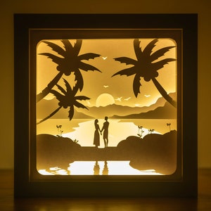 May include: A silhouette of a couple standing on a beach with palm trees and a sunset in the background. The image is illuminated from behind, creating a glowing effect.