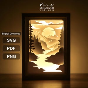 May include: A rectangular shadow box frame containing a layered paper cut-out scene of a river flowing through a forest toward mountains under a large sun. The text "Digital Download", "SVG", "PDF", "PNG", and "MODALIZED VISUALS" is visible.