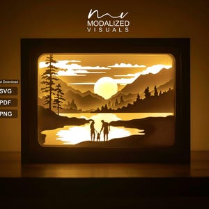 May include: A rectangular shadow box light featuring a layered paper cut-out scene of a family standing by a lake at sunset with mountains and pine trees in the background. The text MODALIZED VISUALS appears at the top, with SVG, PDF, and PNG labels.