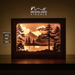 Puede incluir: Una caja de luz rectangular con un paisaje de papel recortado en capas que muestra un bosque, montañas y un lago en tonos naranja cálido y negro. El texto "mv MODALIZED VISUALS" aparece arriba, con "Digital Download SVG PDF PNG" a la izquierda.