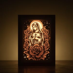 May include: A framed, illuminated artwork depicting a religious figure holding a cross, encircled by roses. The image is a detailed, cut-out design with a warm, glowing light. The artwork is set against a dark background.