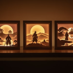 Peut inclure: Trois boîtes à lumière en bois avec des découpes de papier éclairées représentant des scènes japonaises. Chaque boîte présente la silhouette d'une figure en vêtements traditionnels, une pagode et une lune.