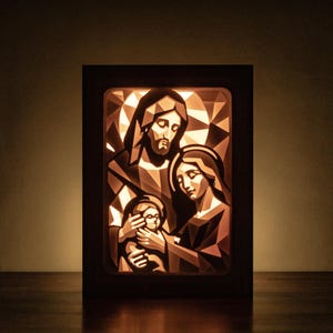 Può includere: Un'opera d'arte incorniciata e illuminata che raffigura una scena religiosa. L'immagine mostra una famiglia con figure geometriche in stile low-poly. L'opera è racchiusa in una cornice di legno scuro, con la fonte di luce dietro le figure, creando un bagliore caldo.