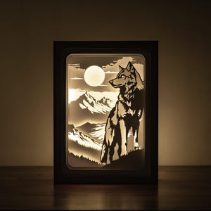 May include: A black framed light-up art piece with a silhouette of a wolf howling at the moon in a mountain landscape.