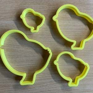 May include: Four yellow plastic chick-shaped cookie cutters in varying sizes. The cutters are made of a solid, bright yellow plastic and are designed with a simple, rounded shape, perfect for Easter or spring-themed baking.