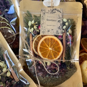 May include: A clear plastic bag filled with dried fruit, herbs, and spices. The bag is tied with twine and has a label that reads "Summer Pot Abundance Sweet Molly Jane's".
