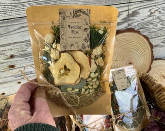 May include: A brown paper bag with a clear plastic window, containing a simmer pot blend. The bag is tied with twine and has a label that reads "Wedding Bliss" with a floral design. The blend includes dried apple slices, flowers, and herbs.
