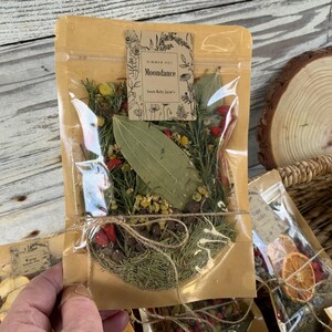 May include: A clear plastic bag filled with dried herbs and spices, including bay leaves, rosemary, and chamomile. The bag is labeled "Summer Pot Moondance Sweet Bath Jewels".