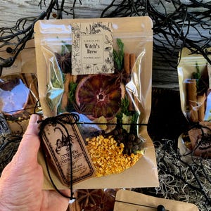 May include: A clear plastic bag filled with dried orange slices, cinnamon sticks, star anise, and other botanicals. The bag has a label that reads "Witch's Brew". A tag with a scorpion illustration is attached.