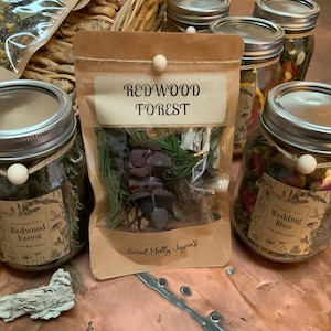 May include: A close-up of three glass jars filled with dried herbs and flowers. The jars are labeled "Redwood Forest", "Wedding Bliss", and "Sweet Molly Jayne's".