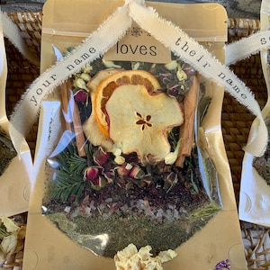 May include: Two brown paper bags with clear plastic windows filled with dried fruit, herbs, and spices. The bags are tied with twine and have labels that say "your name loves their name" and "somebody loves somebody".