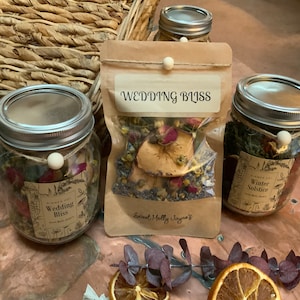 May include: Three glass jars and a small bag filled with dried herbs and flowers. The jars have metal lids and are labeled "Wedding Bliss" and "Winter Solstice." The bag is labeled "Wedding Bliss" and "Sweet Molly Jayne's."