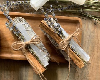 May include: Two bundles of smudging sticks wrapped with twine and lavender. Each bundle includes white sage, palo santo wood, and a clear selenite crystal.