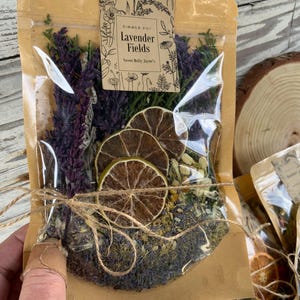 May include: A brown paper bag with a clear plastic window, filled with dried lavender, dried citrus, and other herbs. The bag is tied with twine and has a label that reads "Simmer Pot Lavender Fields Sweet Molly Jayne's".