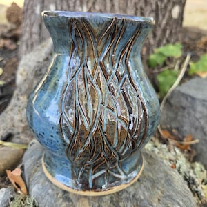 May include: A ceramic vase with a flared rim and a rounded body, featuring a glossy blue glaze with dark brown, carved vertical branch-like patterns that reveal the clay texture beneath, creating a textured surface across the exterior.